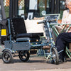 Image of Man and lady sitting with the eFOLDi Explorer Ultra Lightweight Mobility Scooter next to them