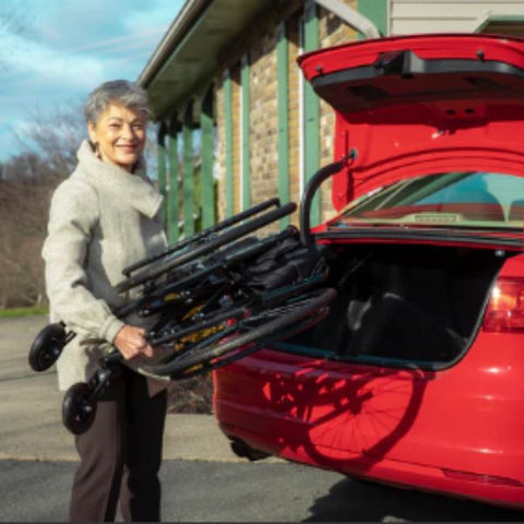 Lady about to put the folded Feather Lightweight Wheelchair in the back trunk of a car