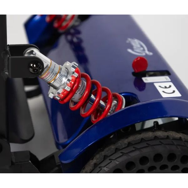 Close-up of the Genie Lightweight Folding Mobility Scooter showing the rear suspension with a red coil spring, shock absorber, black tire, and a red button on the body panel.