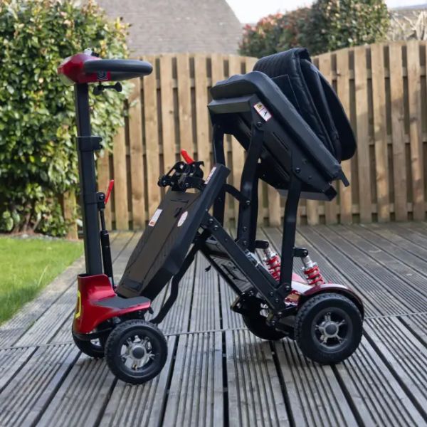 Genie Lightweight Folding Mobility Scooter shown on a wooden deck with a fence and greenery in the background.
