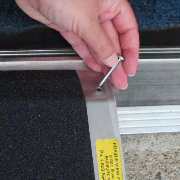 Hand holding a screw near a metal frame of the PVI Aluminum Solid Bariatric Threshold Ramp