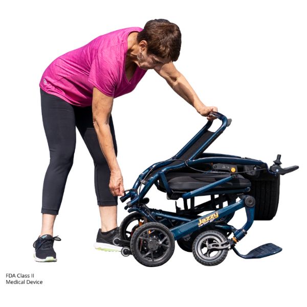 Woman pushing to fold the blue Pride Jazzy Carbon 27 Folding Power Wheelchair on a white background