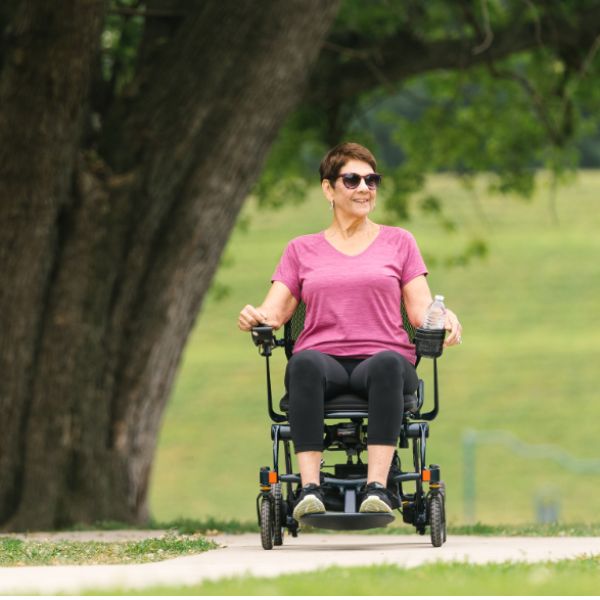 Woman using a Pride Jazzy Carbon 27 power chair in a park setting.