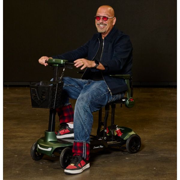 A man wearing red sunglasses, a dark jacket, and jeans sits on the Monarch Mobility Smarti Plus  auto-folding mobility scooter, photographed against a dark studio background.