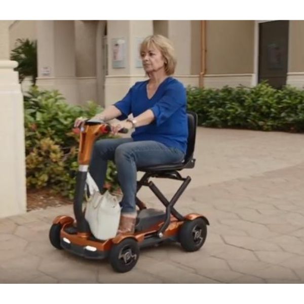 Image of a folding mobility scooter from EV Rider TeQno AF series, shown from the front view with a passenger. The scooter is compact and designed for easy transportation and maneuverability.